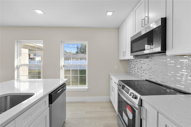 kitchen with stainless steel appliances, light stone countertops, decorative backsplash, and white cabinetry