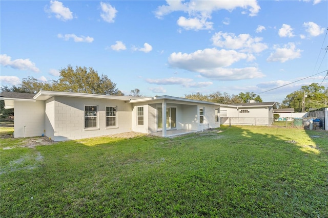 rear view of house featuring a lawn, concrete block siding, and fence