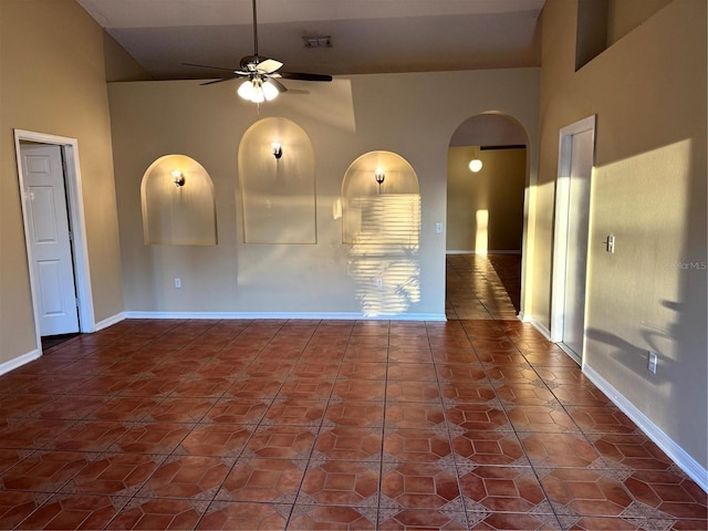 tiled empty room featuring a high ceiling, a ceiling fan, arched walkways, and baseboards