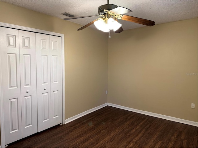 unfurnished bedroom featuring visible vents, dark wood-type flooring, a textured ceiling, a closet, and baseboards