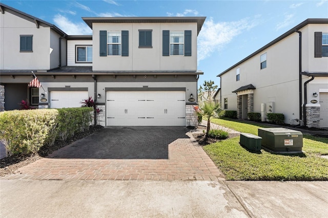 view of property featuring decorative driveway, a garage, stone siding, and stucco siding