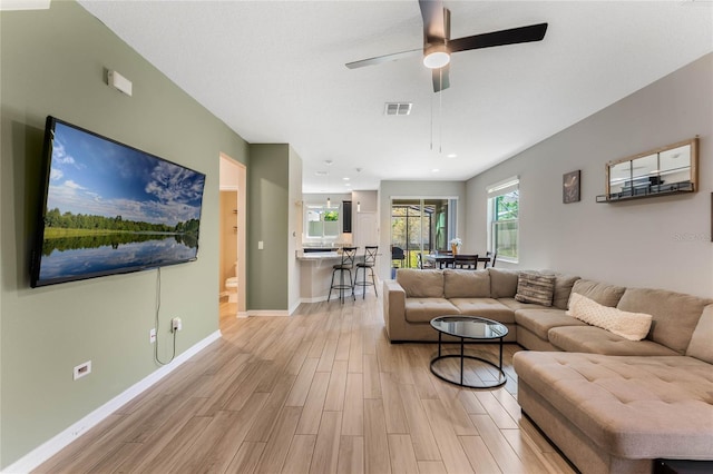 living room featuring ceiling fan, light wood-style floors, visible vents, and baseboards