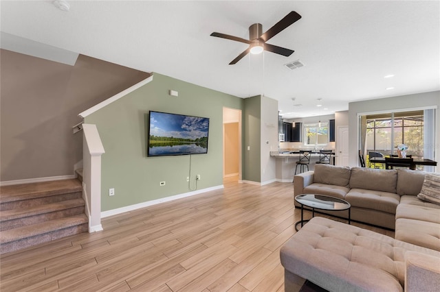 living area with light wood finished floors, visible vents, ceiling fan, baseboards, and stairs