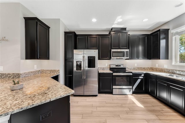 kitchen featuring dark cabinetry, light stone counters, wood tiled floor, and stainless steel appliances