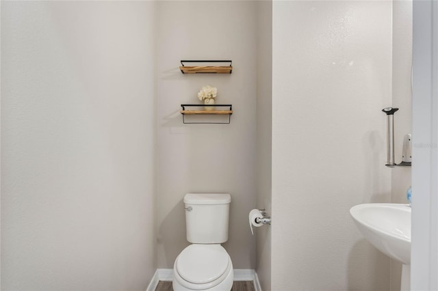 half bath with a sink, baseboards, and toilet