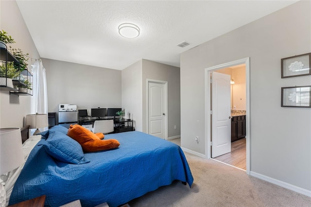 bedroom with visible vents, ensuite bathroom, a textured ceiling, baseboards, and light colored carpet