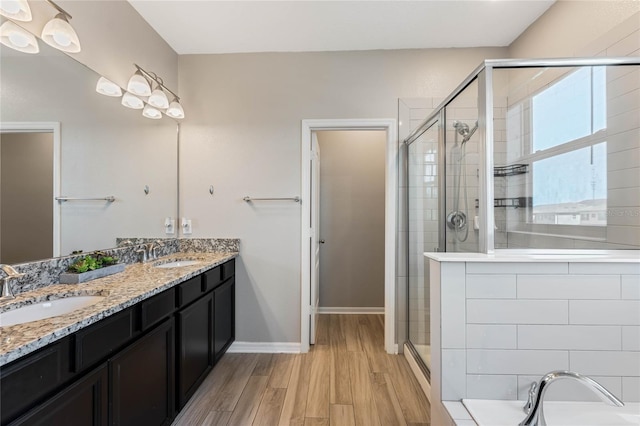 bathroom featuring double vanity, wood finished floors, a stall shower, and a sink