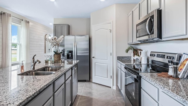 kitchen featuring gray cabinets, a sink, light stone counters, appliances with stainless steel finishes, and light tile patterned flooring