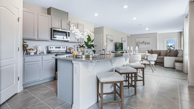 kitchen with a breakfast bar, a center island with sink, light stone counters, stainless steel appliances, and light tile patterned flooring