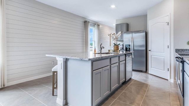 kitchen featuring light tile patterned floors, an island with sink, gray cabinetry, stainless steel appliances, and a sink