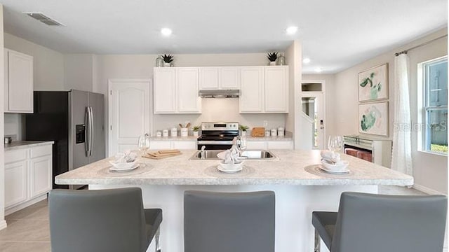 kitchen featuring visible vents, under cabinet range hood, light countertops, appliances with stainless steel finishes, and a kitchen breakfast bar