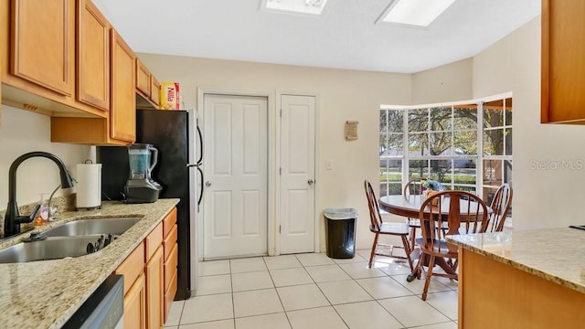 kitchen with brown cabinets, a sink, light stone counters, light tile patterned floors, and dishwasher