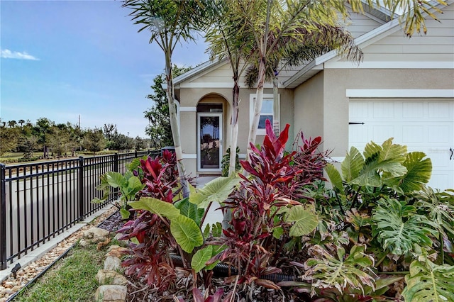 view of exterior entry with stucco siding, a garage, and fence