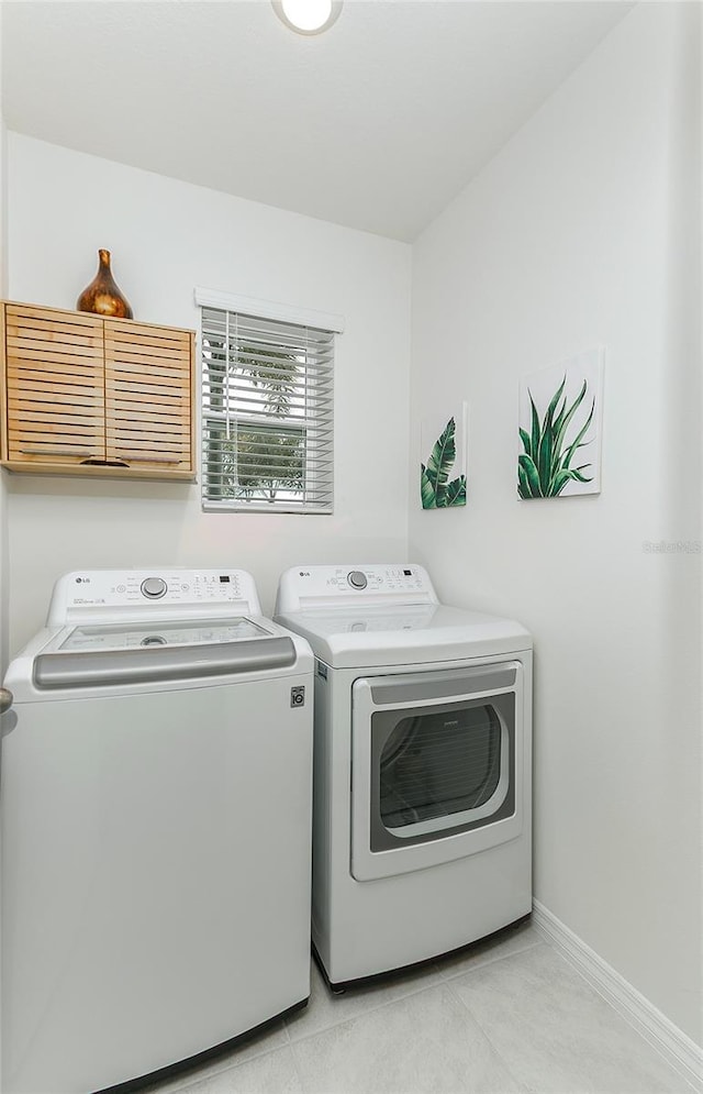 laundry area with light tile patterned floors, washing machine and dryer, cabinet space, and baseboards