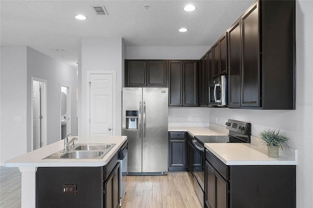 kitchen featuring light wood finished floors, a center island with sink, a sink, appliances with stainless steel finishes, and light countertops