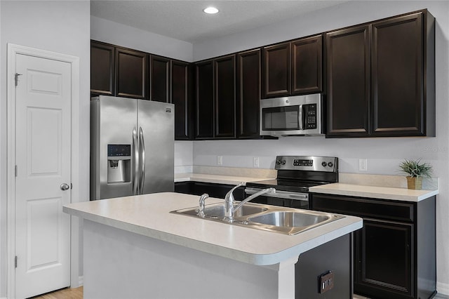 kitchen with an island with sink, a sink, a textured ceiling, appliances with stainless steel finishes, and light countertops