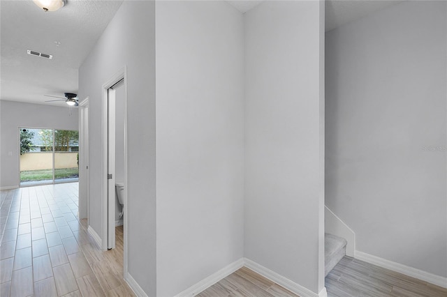 hallway with visible vents, baseboards, and light wood-style floors