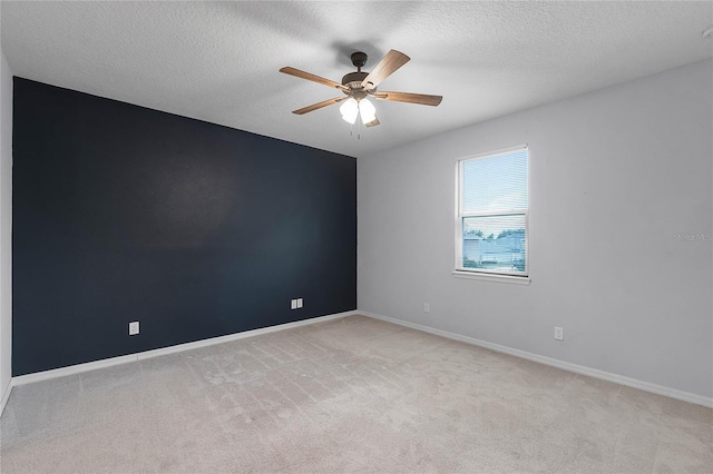 empty room featuring a ceiling fan, light colored carpet, baseboards, and a textured ceiling