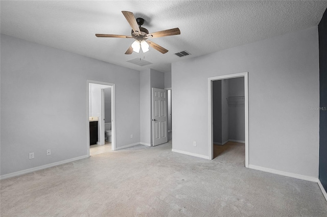 unfurnished bedroom with baseboards, visible vents, a spacious closet, a textured ceiling, and light carpet