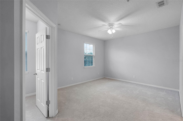 empty room featuring a ceiling fan, baseboards, visible vents, a textured ceiling, and light carpet