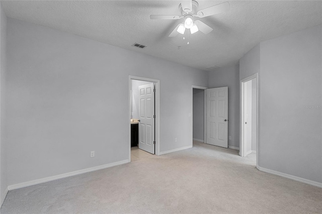 unfurnished bedroom featuring visible vents, baseboards, light carpet, ensuite bathroom, and a textured ceiling