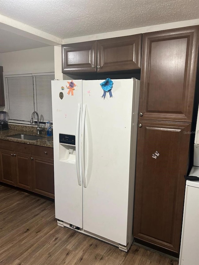 kitchen with dark brown cabinetry, white refrigerator with ice dispenser, dark wood-style floors, a textured ceiling, and a sink