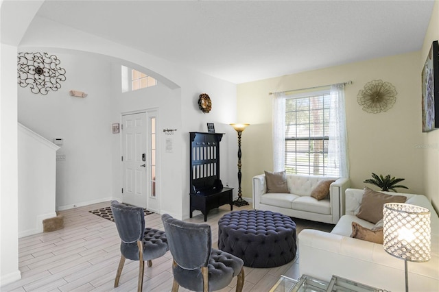 living area with baseboards, arched walkways, and light wood finished floors