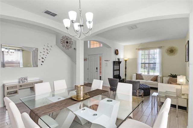 dining space with a chandelier, visible vents, arched walkways, and wood tiled floor