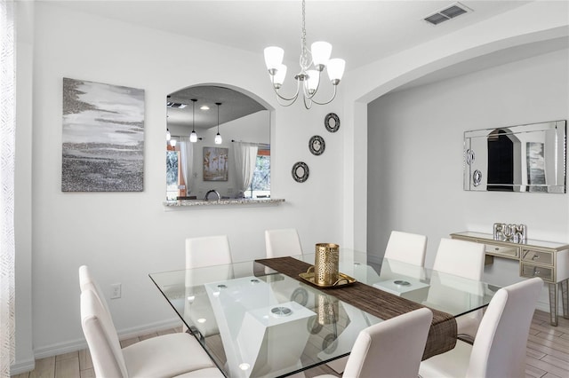 dining area with visible vents, a notable chandelier, wood finished floors, arched walkways, and baseboards