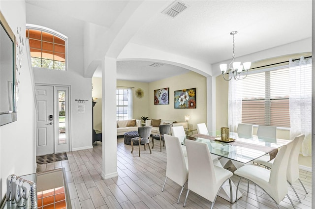 dining area with visible vents, baseboards, wood finish floors, an inviting chandelier, and arched walkways