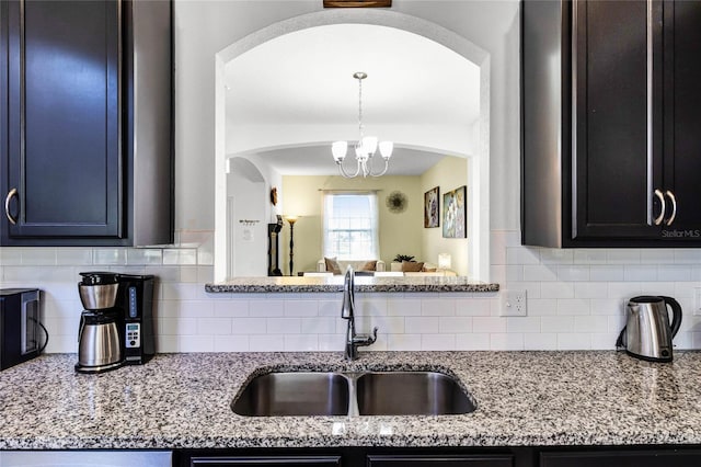 kitchen featuring a notable chandelier, decorative backsplash, light stone countertops, and a sink