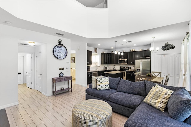 living area with visible vents, baseboards, a high ceiling, and light wood finished floors