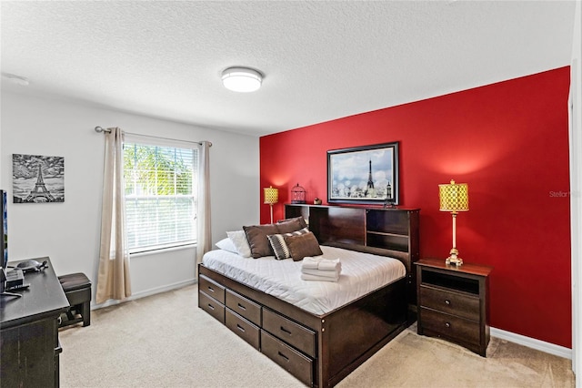 bedroom with light carpet, a textured ceiling, an accent wall, and baseboards