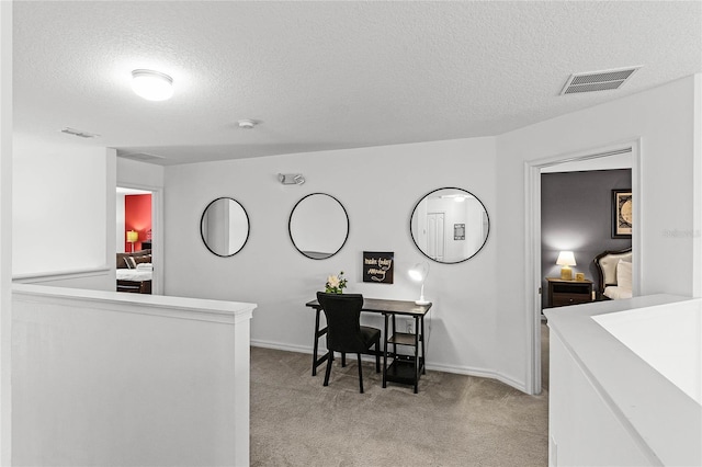 office area featuring a textured ceiling, baseboards, visible vents, and light carpet