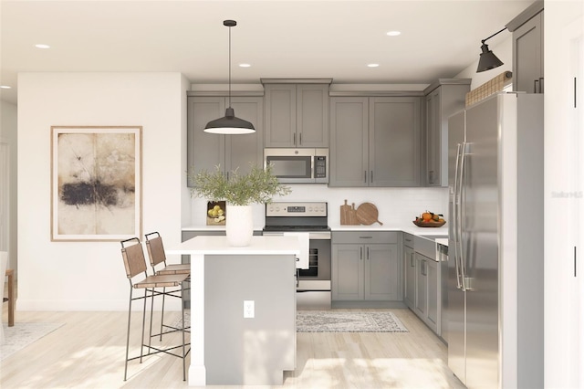 kitchen with a breakfast bar area, gray cabinetry, light countertops, appliances with stainless steel finishes, and a center island