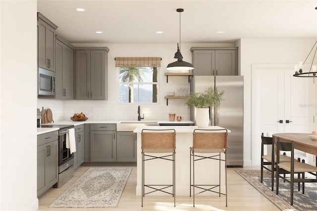 kitchen with backsplash, gray cabinets, light wood-style flooring, stainless steel appliances, and a sink