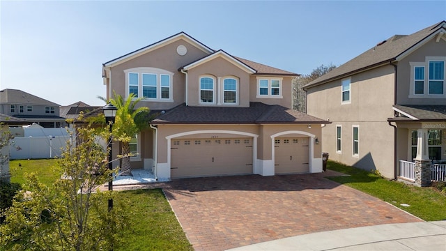 view of front of home featuring a front lawn, fence, stucco siding, decorative driveway, and a garage