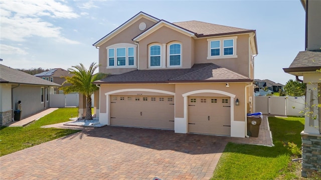 view of front facade with fence, a front yard, stucco siding, decorative driveway, and an attached garage