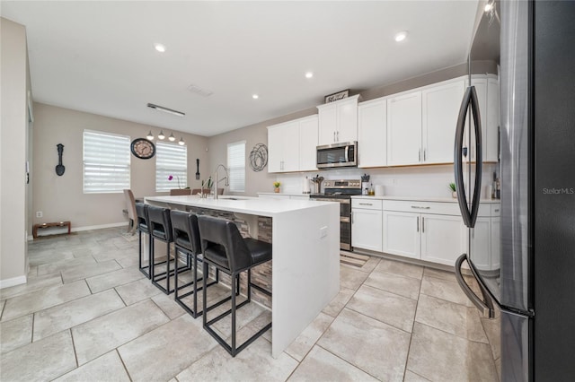 kitchen with a center island with sink, a sink, stainless steel appliances, light countertops, and white cabinets