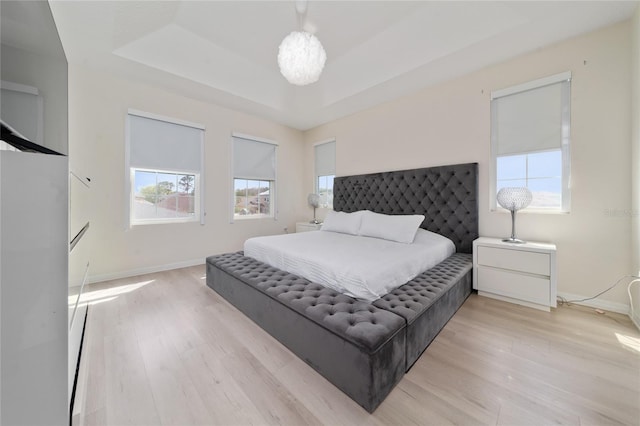 bedroom featuring light wood-style flooring, a raised ceiling, and baseboards