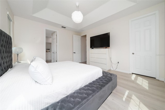 bedroom with visible vents, baseboards, a tray ceiling, light wood-style floors, and connected bathroom