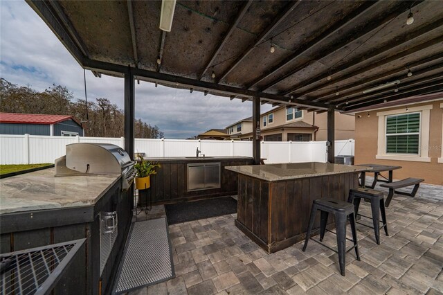 view of patio / terrace featuring outdoor wet bar, exterior kitchen, a fenced backyard, and a sink