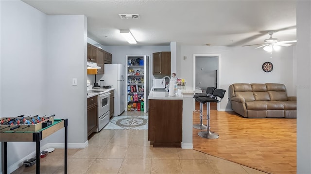 kitchen featuring white appliances, visible vents, under cabinet range hood, a kitchen bar, and open floor plan