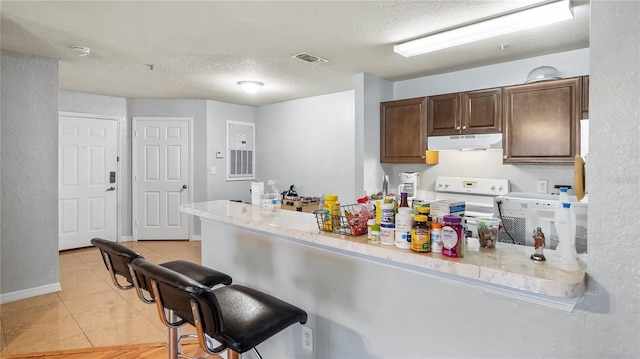 kitchen featuring visible vents, under cabinet range hood, a breakfast bar area, light countertops, and white stove