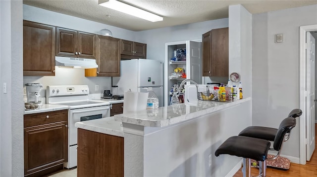 kitchen with under cabinet range hood, white appliances, a peninsula, a breakfast bar area, and light countertops