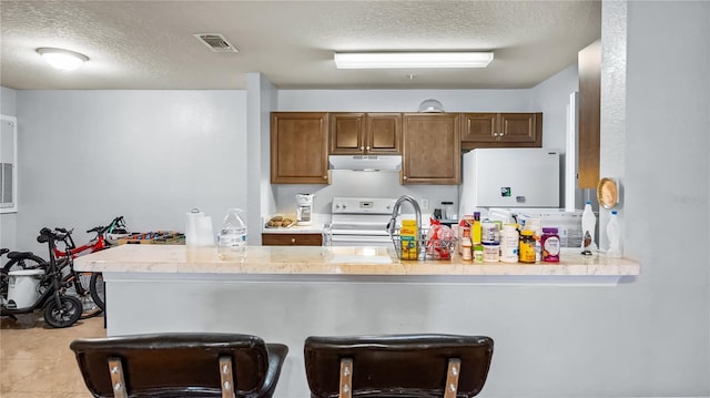 kitchen featuring white appliances, brown cabinetry, visible vents, a peninsula, and under cabinet range hood