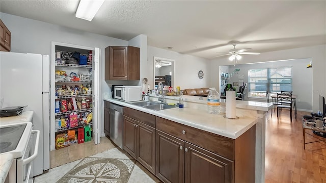 kitchen featuring a ceiling fan, a sink, open floor plan, white appliances, and a peninsula