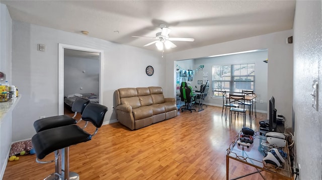 living room featuring baseboards, light wood finished floors, and ceiling fan