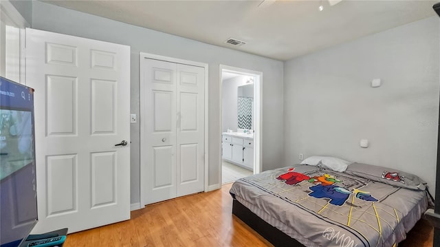 bedroom featuring ensuite bath, a closet, visible vents, and light wood finished floors