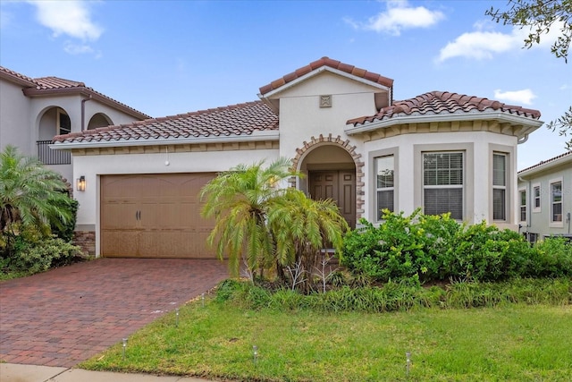 mediterranean / spanish home with decorative driveway, stucco siding, an attached garage, and a tiled roof